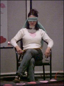 Christine sits blindfolded as the contestants are led onto the Festival stage. In Singled Out, the "date" is not supposed to see the contestants who have not been eliminated, so any time a contestant and the "date" were to be in potential eye contact, Christine got blindfolded.